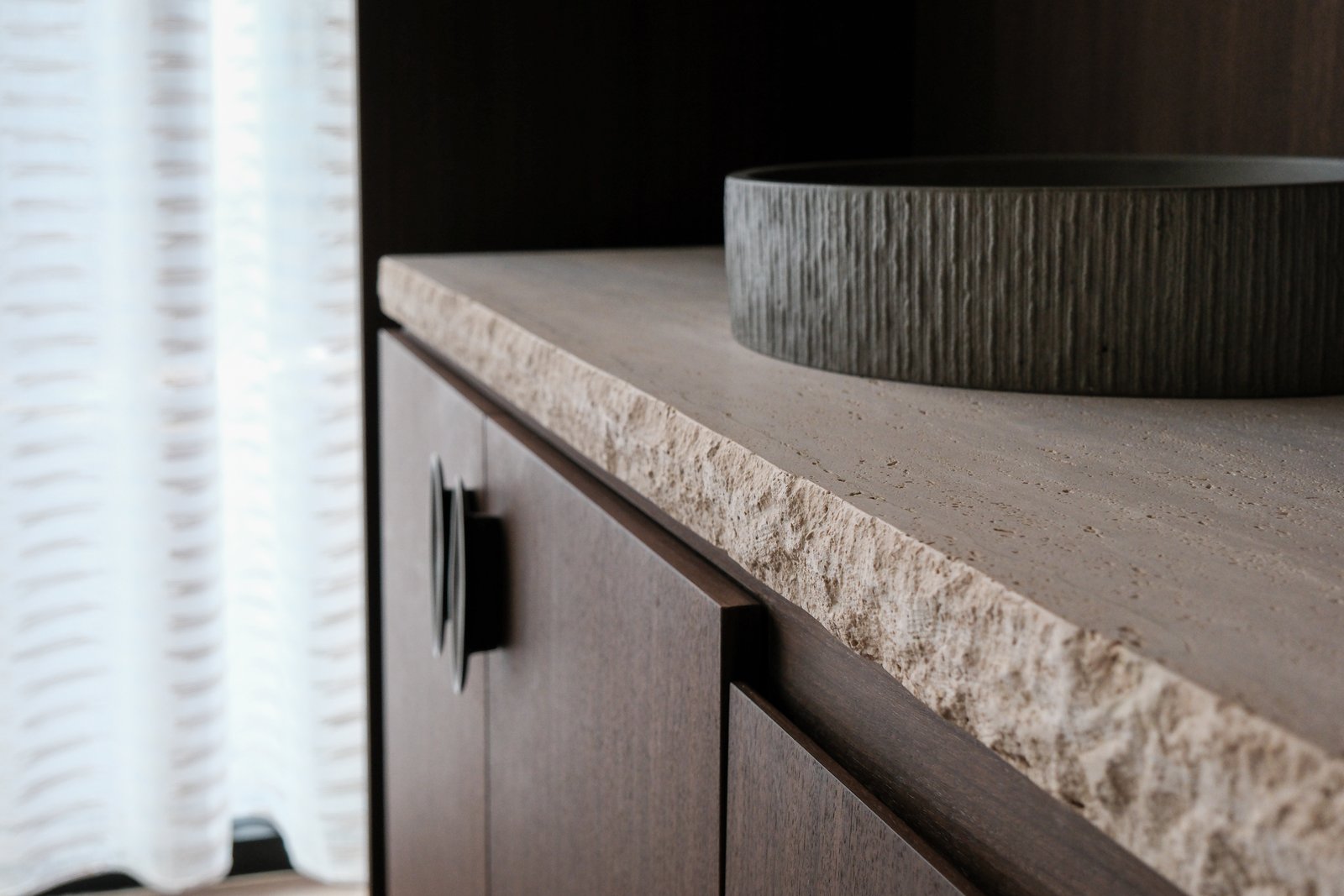 Detail of a chiseled travertine counter edge and fluted stone basin at the bluSONIL studio