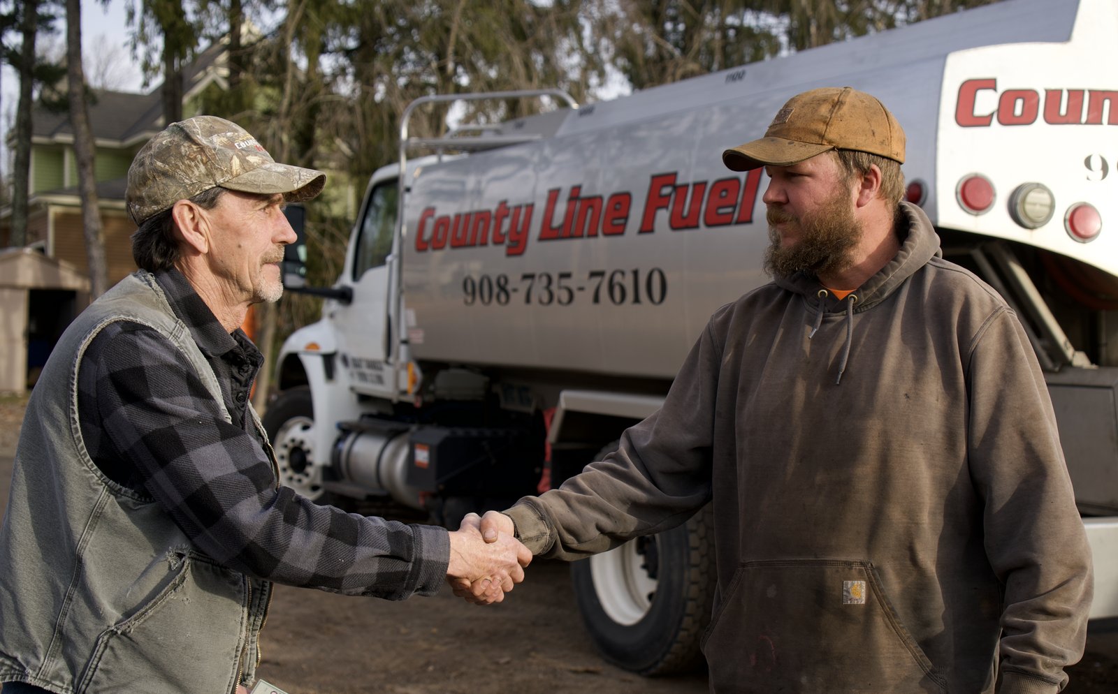 A fuel delivery driver and a customer shaking hands in front of the delivery truck