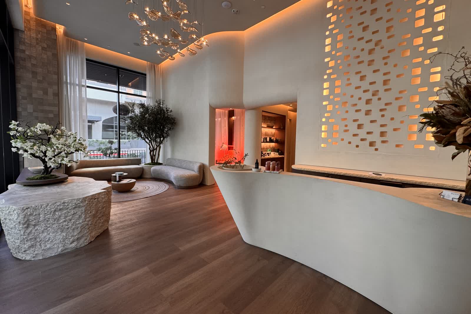 The finished lobby at bluSONIL Scottsdale, with a cherry blossom tree on a stone block, an olive tree in a built in planter, curved seating and the reception desk, empty